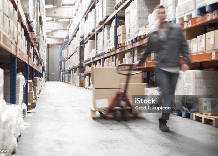 A young man using a pallet truck to move stock in a storehouse